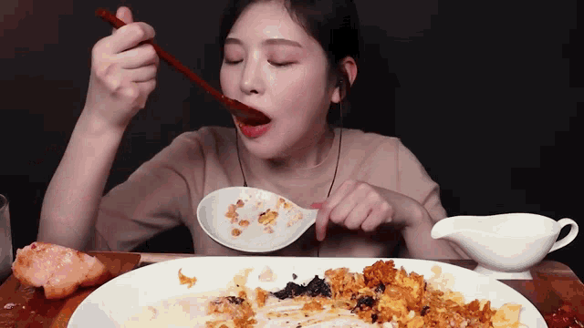 a woman is eating a plate of food with a spoon and chopsticks .