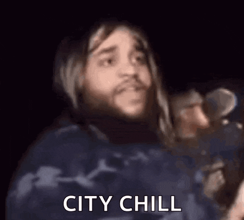 a man with long hair and a beard is holding a microphone and saying city chill .