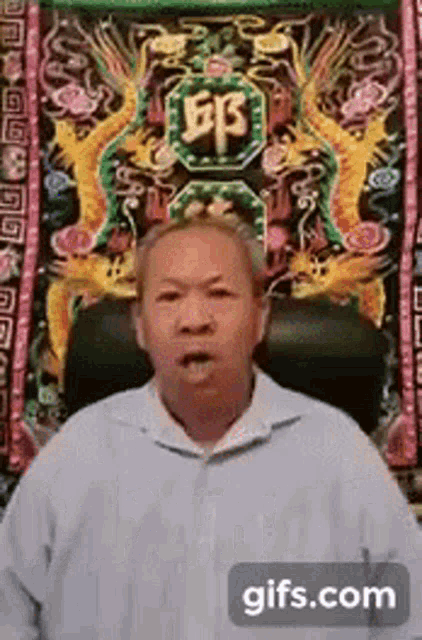 a man is sitting in front of a colorful tapestry with chinese characters on it .