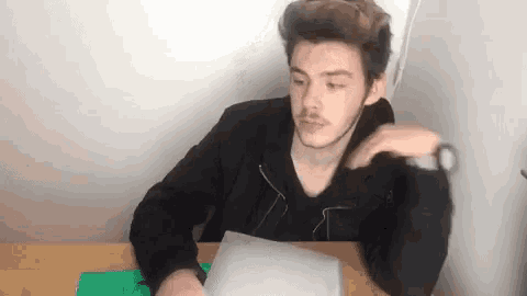 a young man is sitting at a table holding a pair of scissors and a piece of paper .