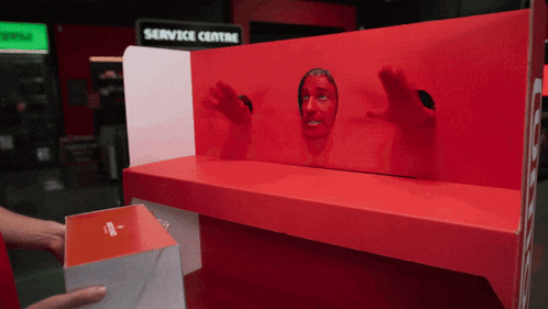 a man is sticking his head through a hole in a red box with a service centre sign in the background