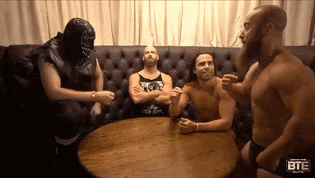 a group of wrestlers are sitting around a table with the bte elite logo on the bottom