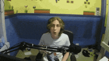 a young man is sitting in front of a microphone in a room with a yellow wall