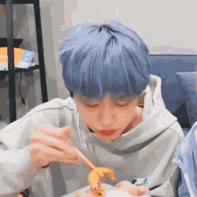 a young boy with blue hair is eating a shrimp with chopsticks .