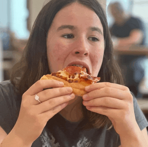 a woman eating a slice of pizza with a ring on her finger