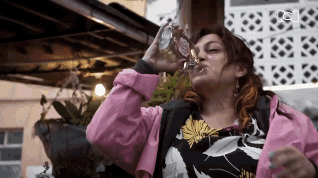 a woman wearing a pink jacket drinks from a glass
