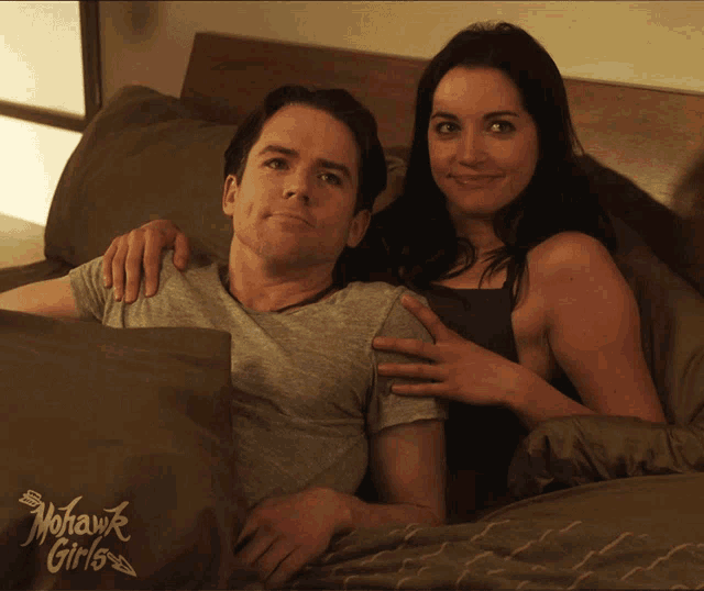 a man and woman are laying on a bed with a nohawk girls pillow