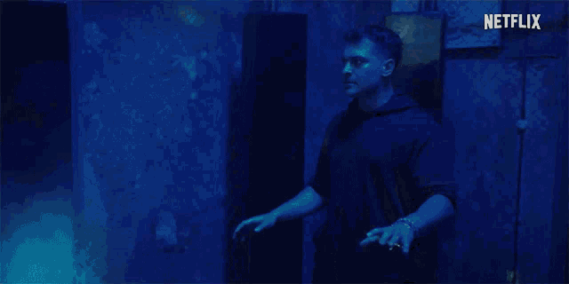 a man in a black hoodie is standing in a dark room with a netflix logo in the background .