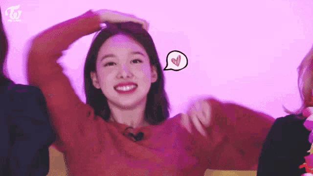 a woman in a red sweater is smiling and holding her hair in front of a pink background .