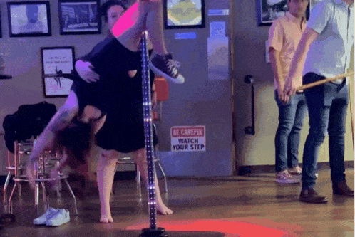 a pole dancer performs in front of a be careful watch your step sign
