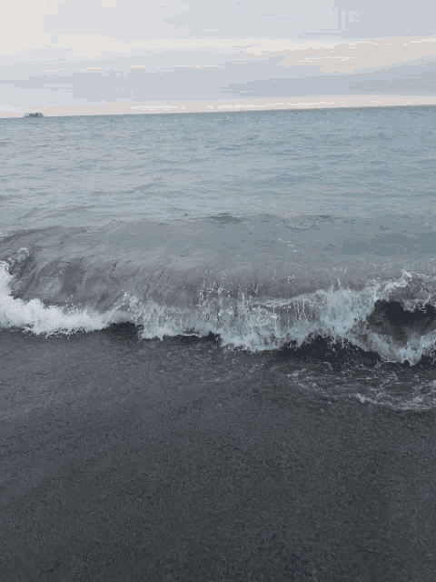 waves crashing on a beach with a boat in the background