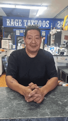 a man sits at a counter in front of a rage tattoos sign