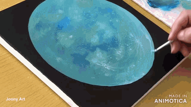 a person is painting a blue moon on a black canvas