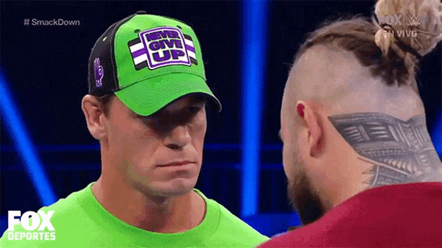 a man wearing a green hat that says give up is looking at another man