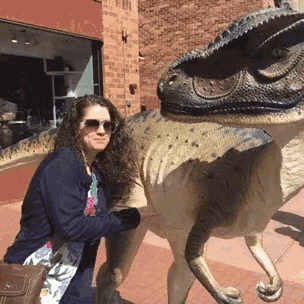 a woman kneeling down next to a dinosaur statue
