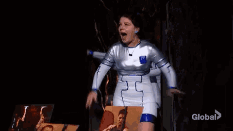 a woman in a space suit is standing on a stage holding a picture of a man .