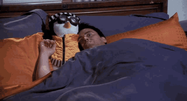 a man is laying in bed with a stuffed penguin