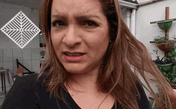 a woman is making a funny face in front of a wall with plants