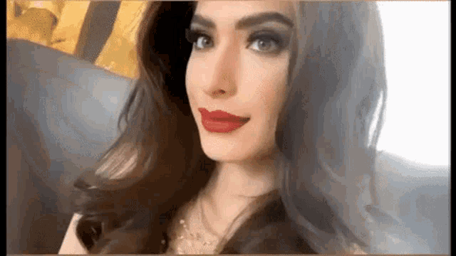 a woman with long brown hair and red lipstick is sitting on a couch .
