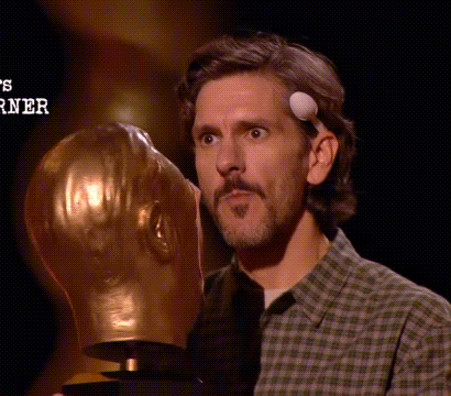 a man in a plaid shirt is holding a trophy with a ball on his forehead .