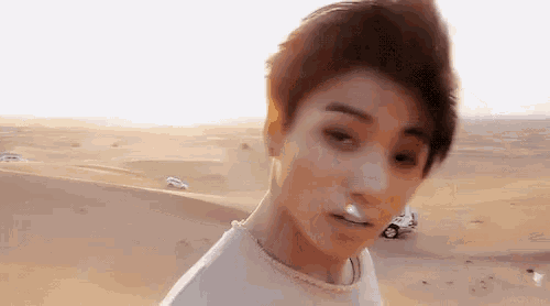 a young man is standing in the desert with a car in the background .