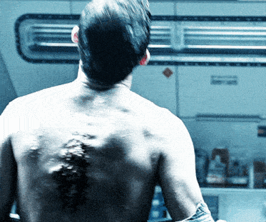 a man without a shirt is standing in front of a sign that says ' emergency exit '