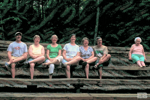 a group of people sitting on a wooden bench with one wearing a shirt that says ' columbia '
