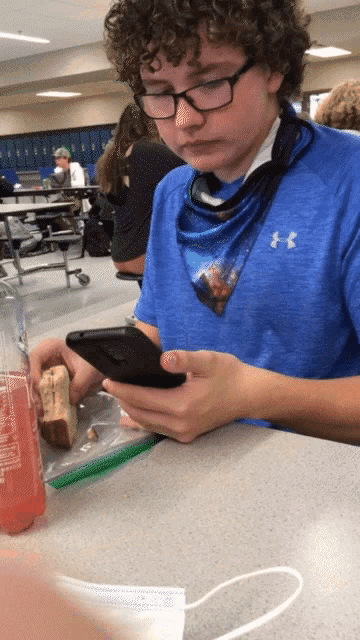 a boy wearing a blue under armour shirt is looking at his cell phone