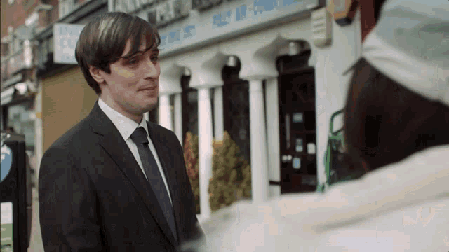a man in a suit and tie talks to a woman in front of a building that says post air conditioning