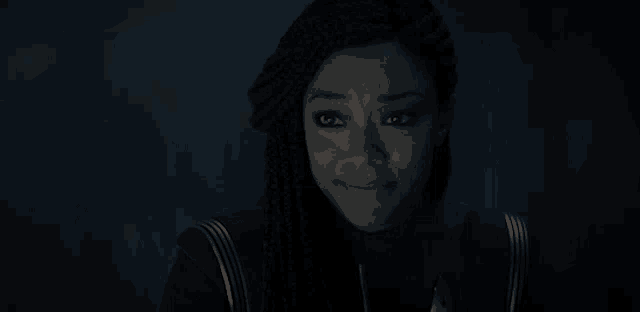 a close up of a woman with braids smiling in the dark