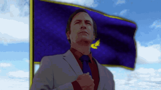 a man in a suit and tie stands in front of a purple flag with a yellow star on it
