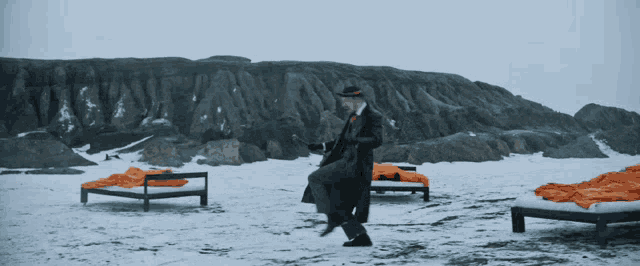 a man in a black coat and hat is standing in the snow near a bed