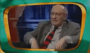 a man in a suit and tie is sitting in front of a television screen with the words wir mussen ficken written on it