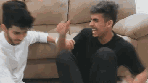 two young men are sitting on the floor in front of a couch giving each other high fives .