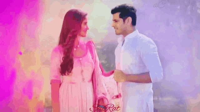 a man and a woman are standing next to each other in front of a pink background .