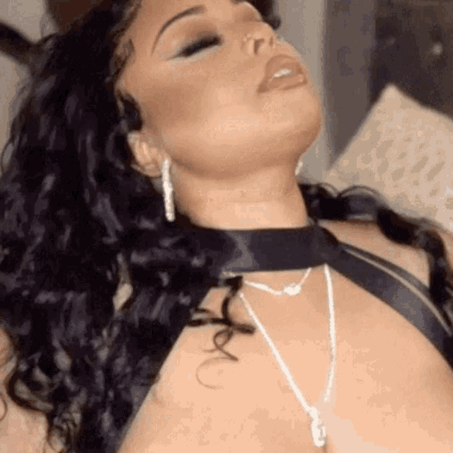 a woman is laying on a bed with her eyes closed and wearing a choker necklace .