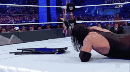 a wrestler is laying on the floor in a wrestling ring with a chair in the background