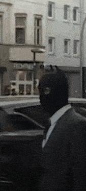 a man in a suit and tie wearing a black mask is walking down the street