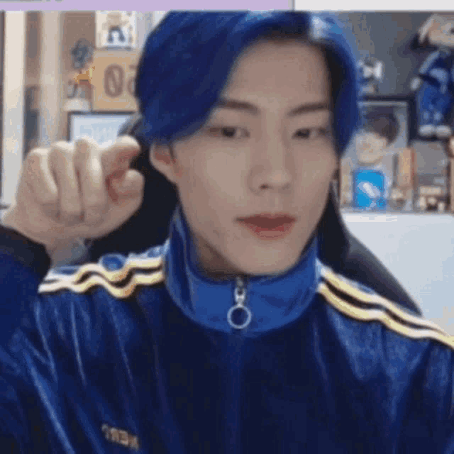 a man with blue hair is wearing a blue jacket and giving a thumbs up sign .