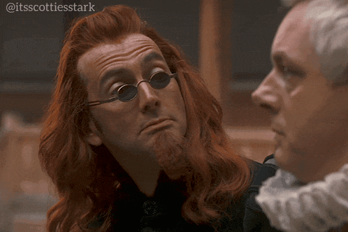 a man with red hair and a beard wearing sunglasses looks at another man