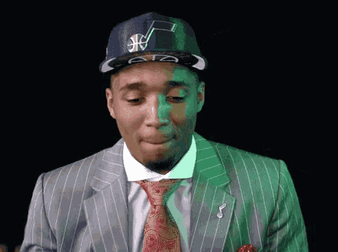 a man in a suit and tie is wearing a hat with a basketball logo on it
