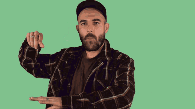 a man with a beard wearing a plaid shirt and a hat holds his hands out