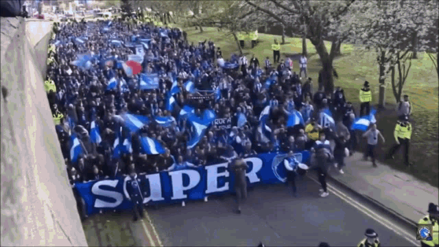 a crowd of people marching down a street with a banner that says super