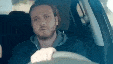 a man is sitting in the driver 's seat of a car looking out the window .