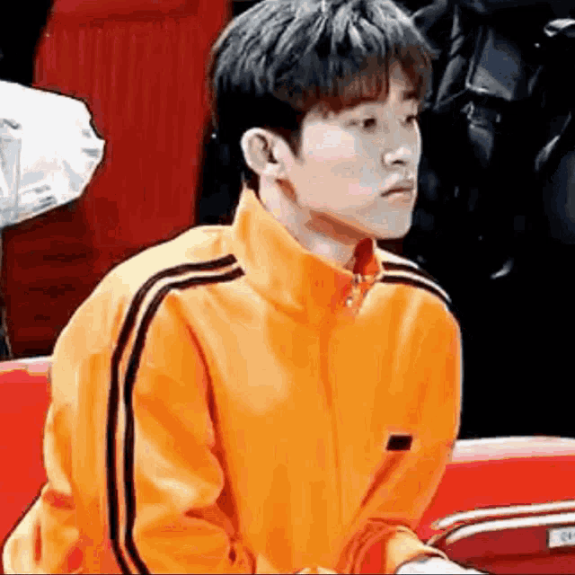 a young man wearing an orange jacket with black stripes is sitting on a red chair .