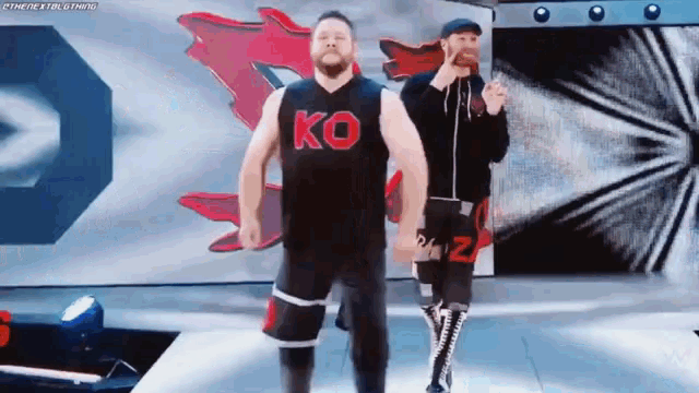 a man in a ko shirt is walking on a stage with a man in a black shirt .