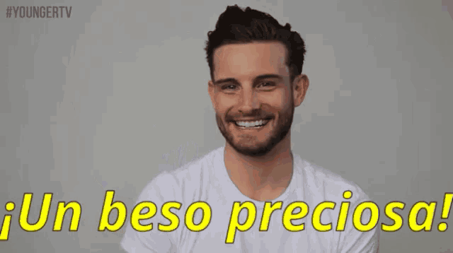 a man in a white t-shirt is smiling and waving with the words un beso preciosa below him