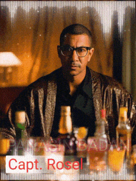 a man sitting at a table with bottles of alcohol and the name capt rosel