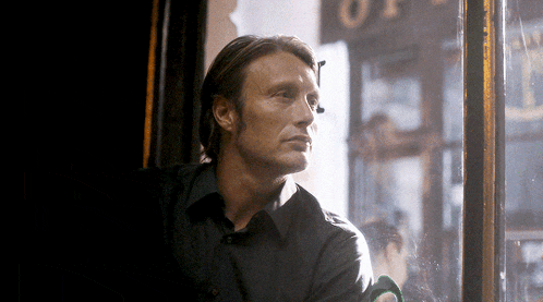 a man in a black shirt looks out a window in front of a sign that says ' op '