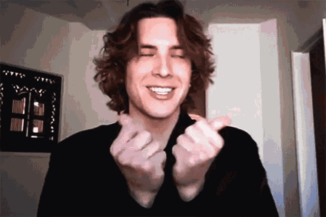 a man with curly hair is smiling and making a heart shape with his hands